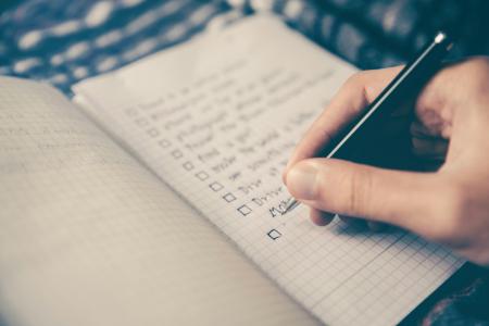 Close up of a person's hand drafting a checklist, with checkboxes, in their notebook.