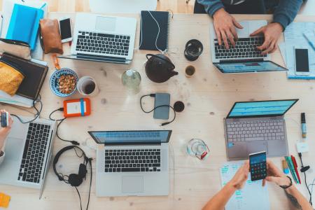 Table with people working on several laptops with phones, tablets. and snacks
