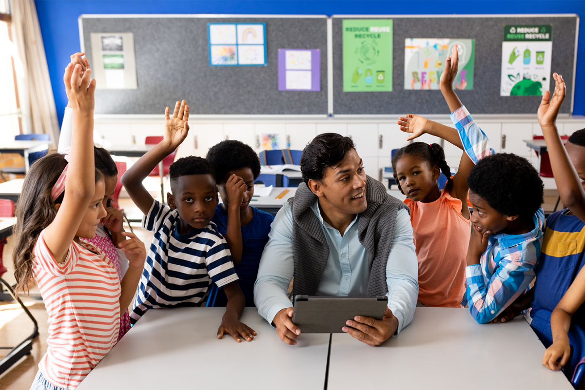 Teacher asking questions to children gathered around him, some kids raising their hands