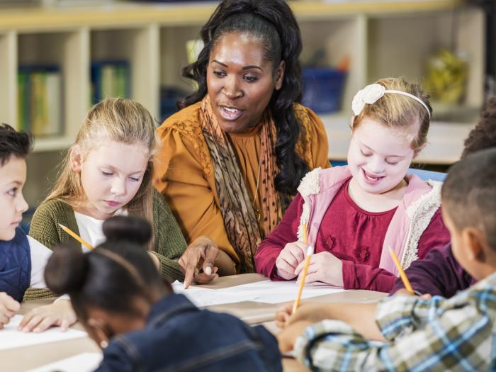 Illinois Special Education Teacher Tuition Waiver Program - Teacher and young students at a table working together on writing