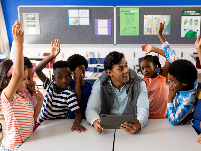 Teacher asking questions to children gathered around him, some kids raising their hands